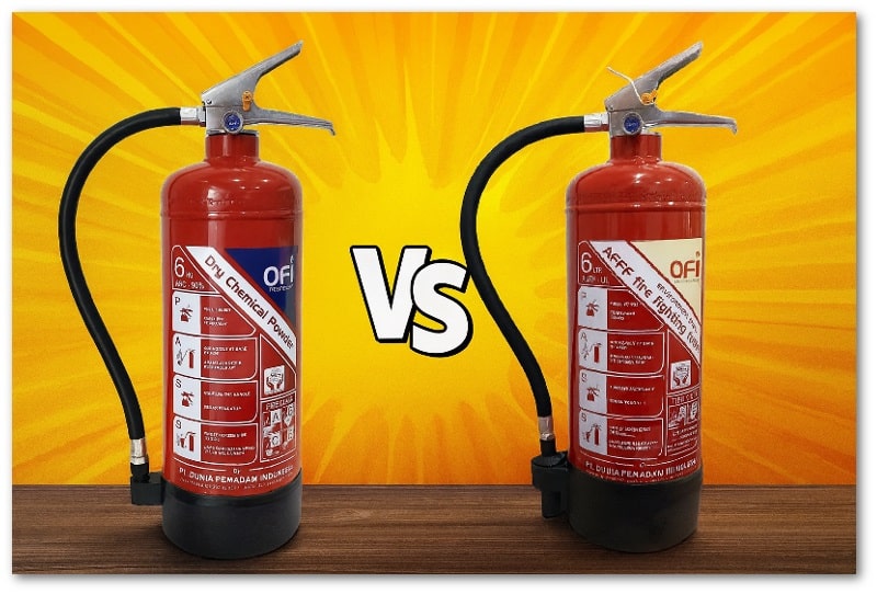 Dua tabung APAR OFI tipe Dry Chemical Powder dan AFFF Foam berdiri berdampingan di atas permukaan kayu, dengan latar belakang gradasi kuning-oranye dan tulisan ‘VS’ di tengah