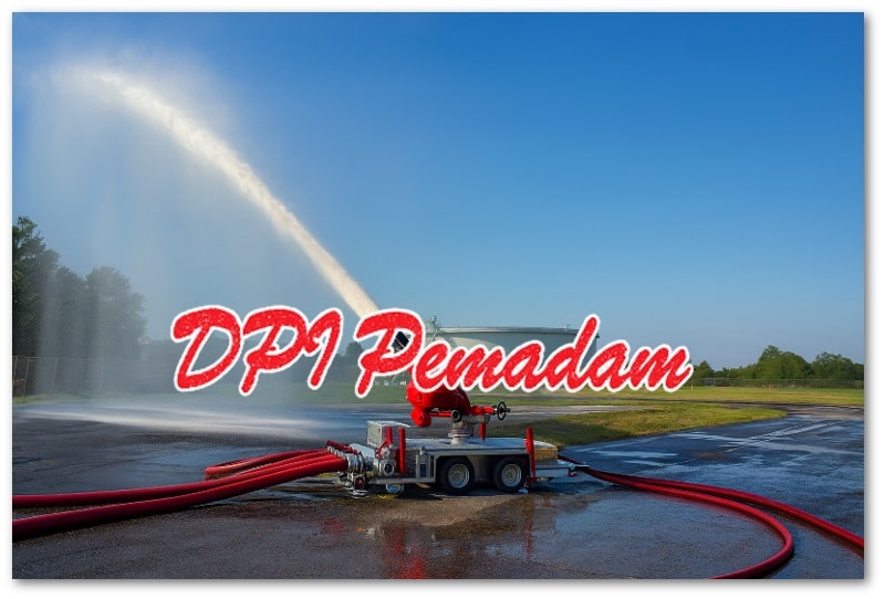 Sebuah monitor pemadam kebakaran berwarna merah yang dipasang pada platform beroda sedang menyemprotkan jet air kuat ke arah kiri, berada di area latihan pemadaman dengan lanskap lapangan hijau dan langit biru cerah.